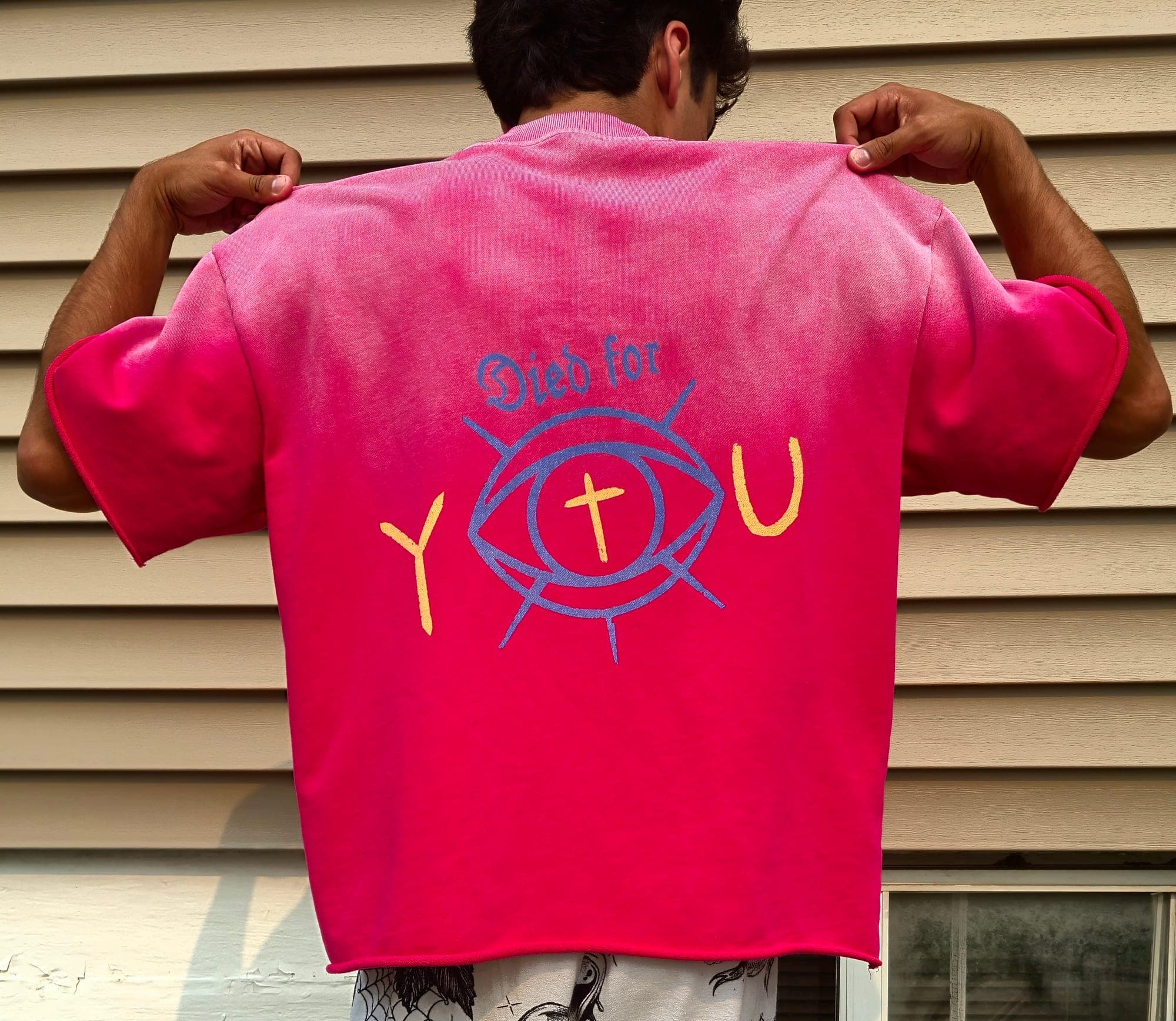 The back of the pink Died for You boxy tee: an eye with a gold cross for a pupil forming the O in YOU