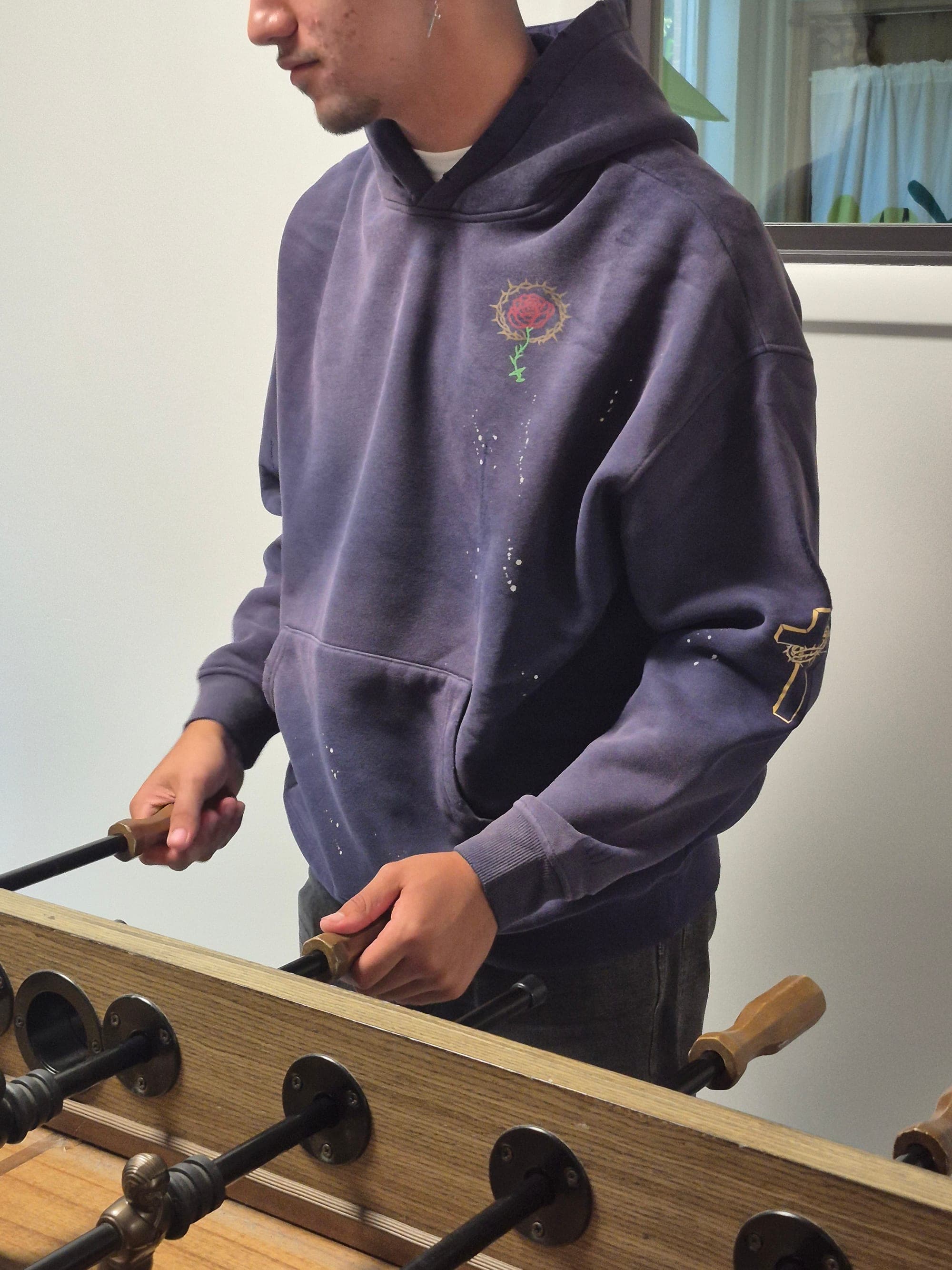 A man in a washed navy Living Water hoodie with a rose in a crown of thorns on the chest and a cross on the sleeve