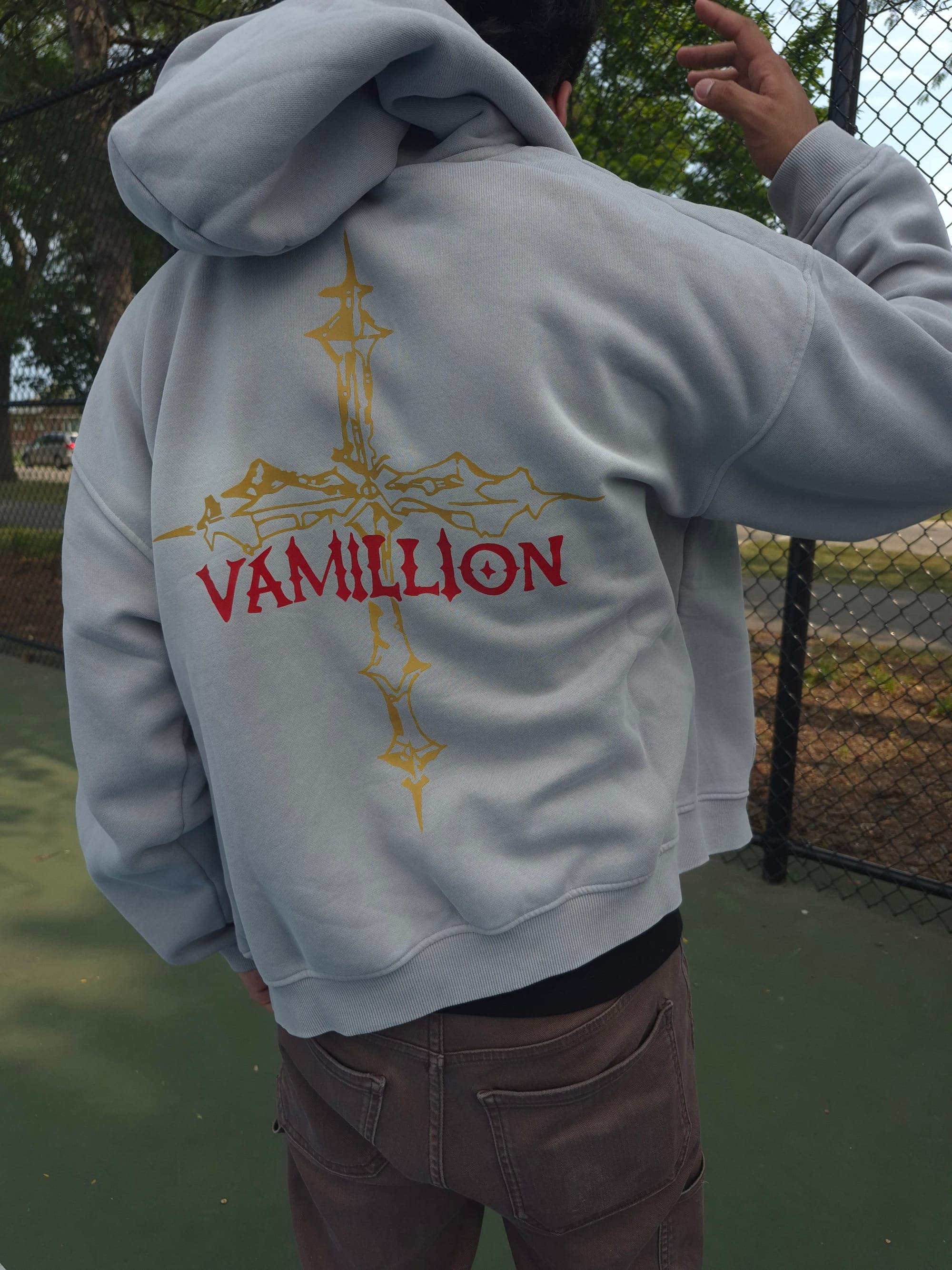The back of a gray VAMILLION hoodie: a gold gothic cross with VAMILLION in red across it